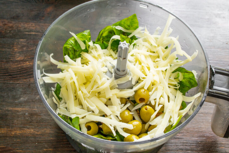 Adding hard cheese like Parmesan to the pesto mix Pieces of hard, salty cheese being added to the blender bowl.