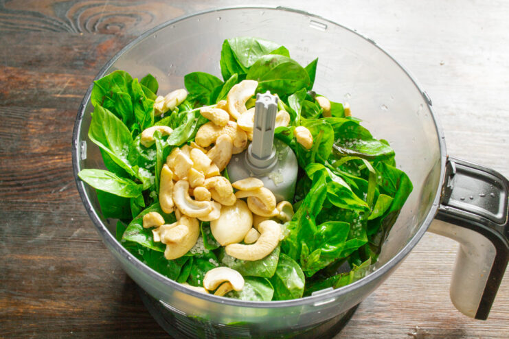 Adding nuts to the pesto ingredients A handful of toasted cashews or pine nuts being added to the blender with basil and garlic.