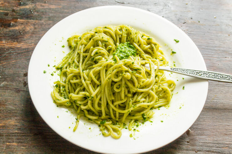 Mixing cooked spaghetti with butter and pesto Cooked spaghetti in a pot being mixed with a generous amount of green pesto sauce.