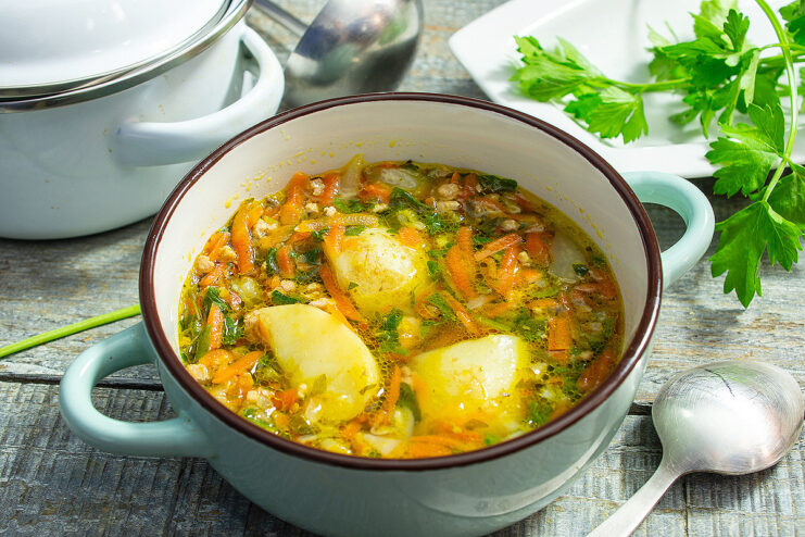 A bowl of finished ground meat and potato soup, garnished with a dollop of sour cream and fresh herbs.