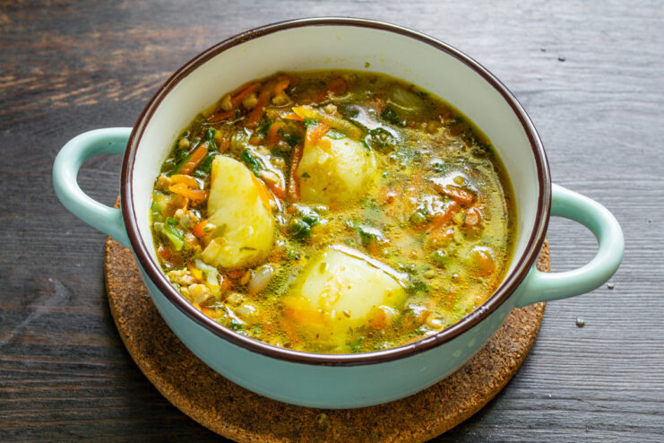 Serving the delicious soup with a dollop of smetana and a sprinkle of pepper. A bowl of hot ground meat and potato soup being garnished with a spoonful of sour cream.