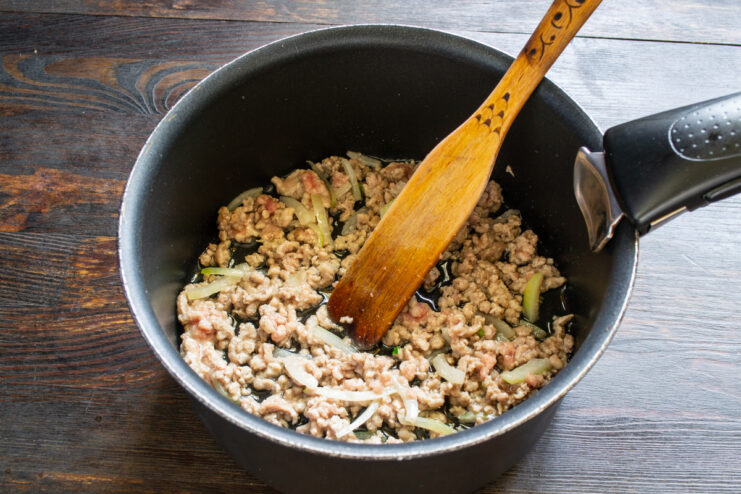 Browning the ground meat with aromatics until cooked through. Ground meat browning in a pot with sautéed onions and garlic.