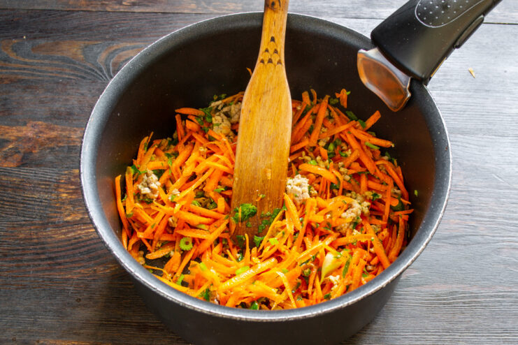 Grated carrots add sweetness and color to the soup. A hand grating a fresh carrot on a box grater over a cutting board.