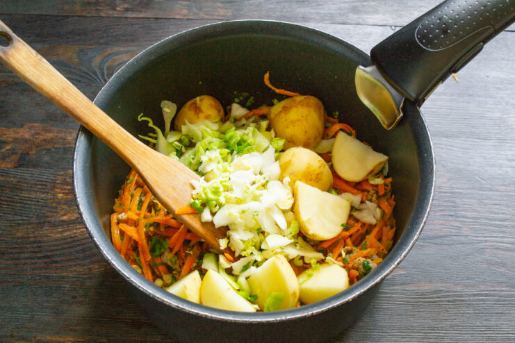 Adding hearty potatoes and cabbage to make the soup filling. Chopped potatoes and shredded cabbage being added to the pot with the meat and vegetables.
