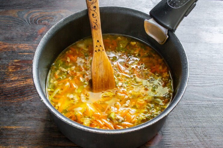 Simmering the soup until all the vegetables are perfectly tender. The ground meat and vegetable soup simmering in a large pot on the stove.