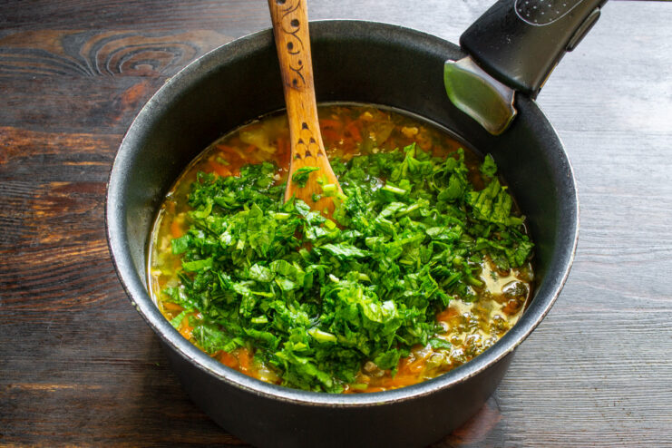 Adding fresh spinach at the end for extra nutrients and color. Fresh spinach being added to the simmering soup in the pot.