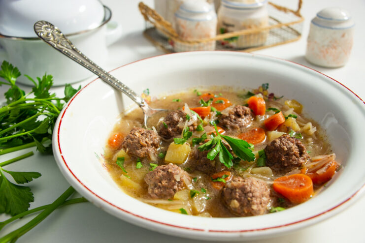 A bowl of finished meatball and walnut soup, garnished with fresh herbs and a dollop of sour cream.