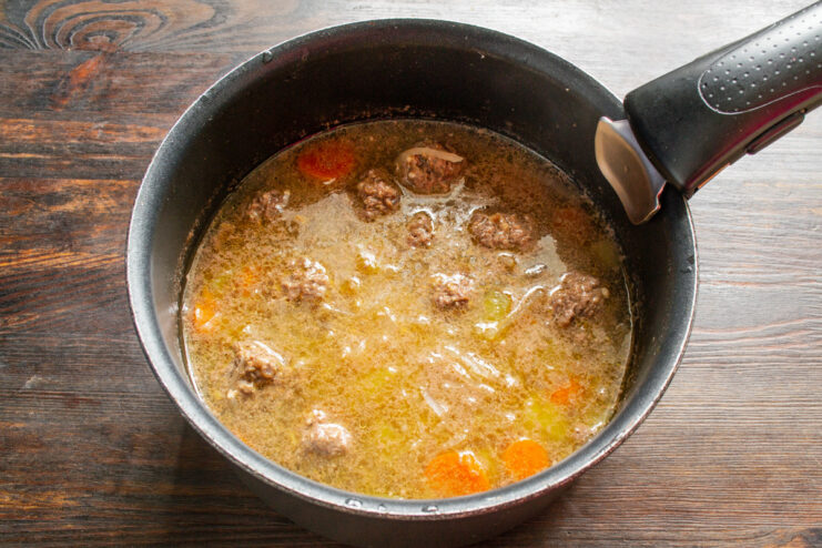 Simmering the soup after adding the meatballs to cook them through Meatball and vegetable soup simmering in a pot on the stove.