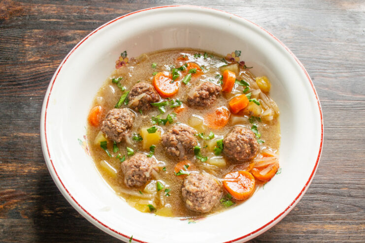 Serving the finished Meatball and Walnut Soup with fresh herbs and smetana A bowl of hot meatball and walnut soup being garnished with fresh herbs and a spoonful of smetana.