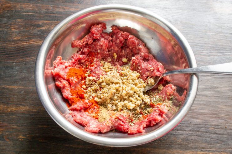Adding crushed walnuts to ground beef for extra flavor and texture Adding crushed walnuts from a mortar into a bowl with seasoned ground beef.
