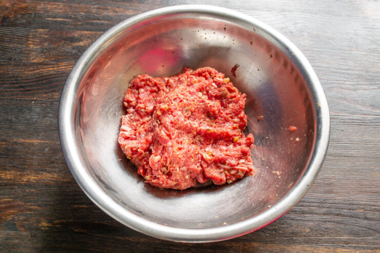 How to properly mix ground meat for tender meatballs Hands mixing ground beef, spices, and walnuts in a glass bowl.