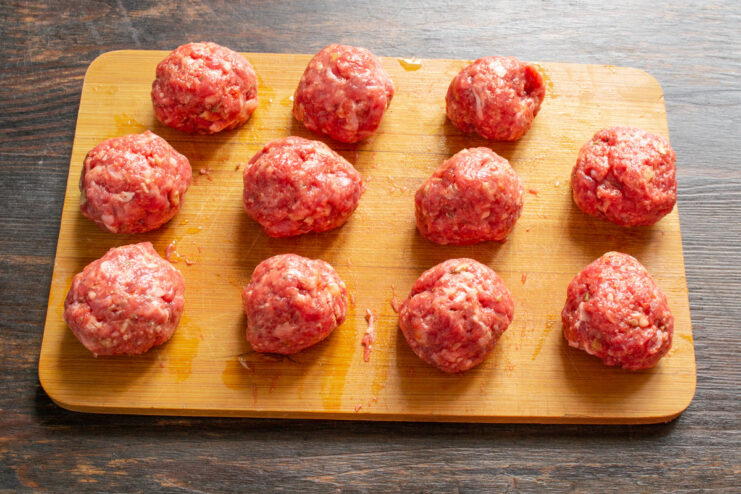 Shaping the perfect walnut-sized meatballs for the soup Raw, perfectly shaped meatballs on a wooden cutting board.