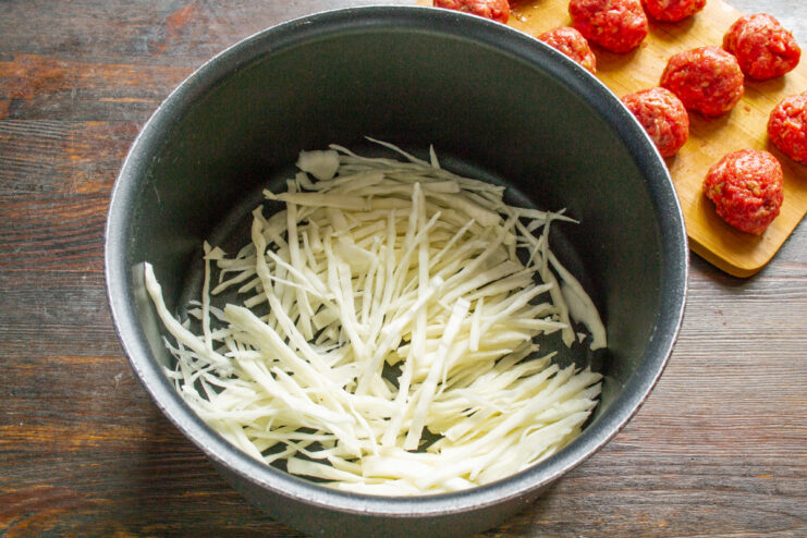 Preparing fresh cabbage for the meatball soup A pile of thinly sliced white cabbage on a cutting board.