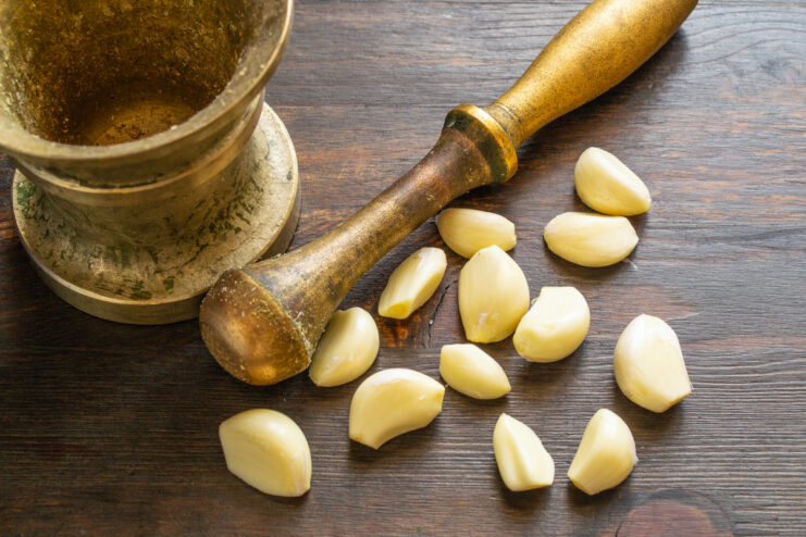 Preparing the Garlic for the Spice Blend A whole head of garlic and several peeled cloves on a wooden surface.