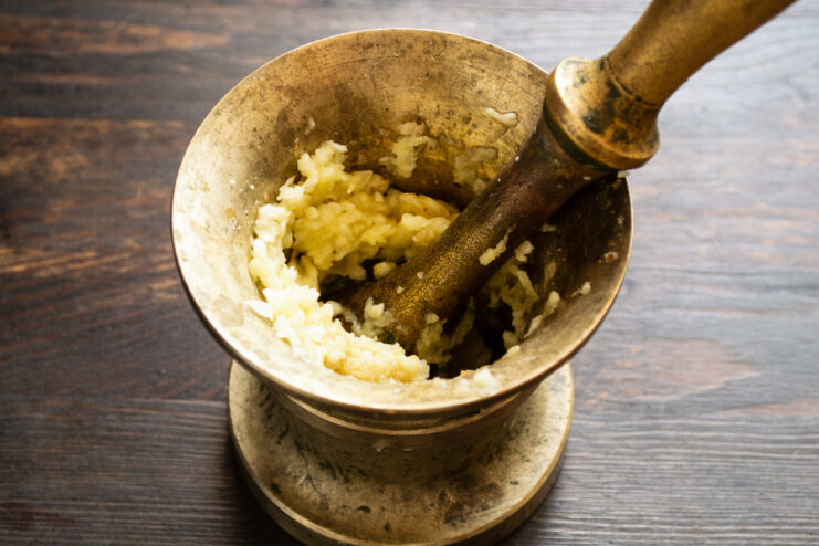 Grinding Garlic into a Paste with a Mortar and Pestle A hand using a pestle to grind garlic cloves into a paste inside a stone mortar.