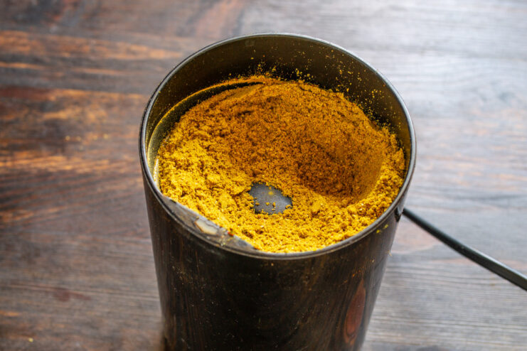 Grinding the Spices into a Fine Powder A collection of whole spices being poured into an electric spice grinder.