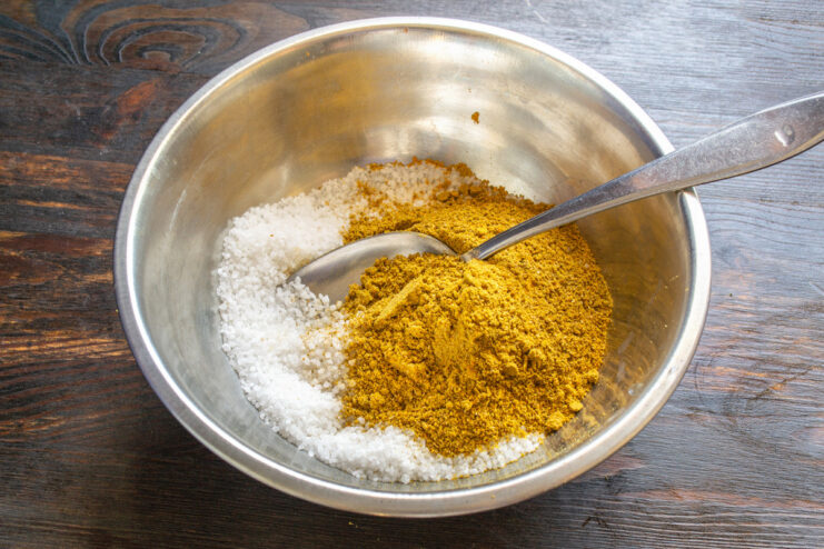 Combining Ground Spices with Sea Salt A spoonful of freshly ground aromatic spices being added to a bowl of coarse sea salt.