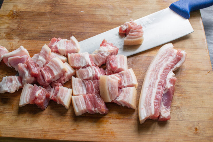 How to Prepare Pork Belly for a Flavorful Rice Dish Raw pork belly being sliced into pieces on a cutting board.
