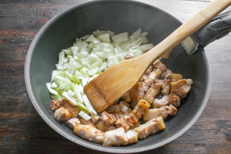 Sautéing Onions Alongside Pork Belly for Maximum Flavor Chopped onions being added to a skillet next to pieces of seared pork belly.