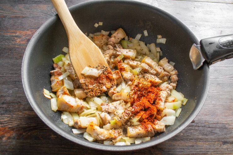 Adding Carrots to the Pork and Onion Base Sliced carrots being added to the skillet with pork belly and onions.