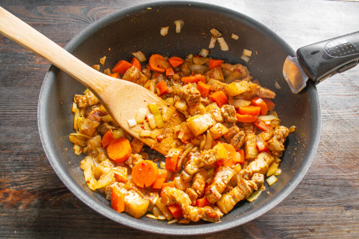 Adding Rinsed Rice to the Skillet with Pork and Vegetables Rinsed white rice being poured into the skillet with the cooked pork and vegetables.