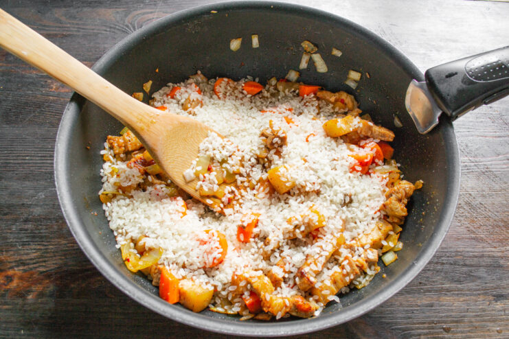 Incorporating Rice into the Pork and Vegetable Mixture White rice being stirred into the mixture of pork belly, onions, and carrots in a skillet.