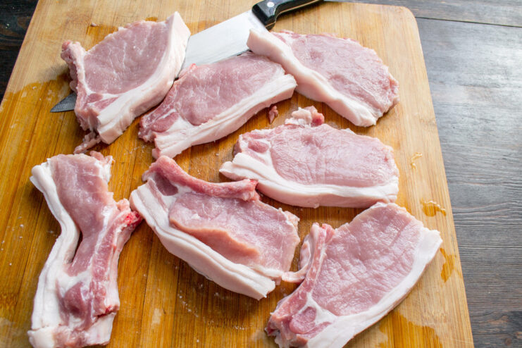 Step 1: Slicing the Pork Loin into Individual Chops Raw pork loin on the bone being sliced into individual chops on a cutting board.