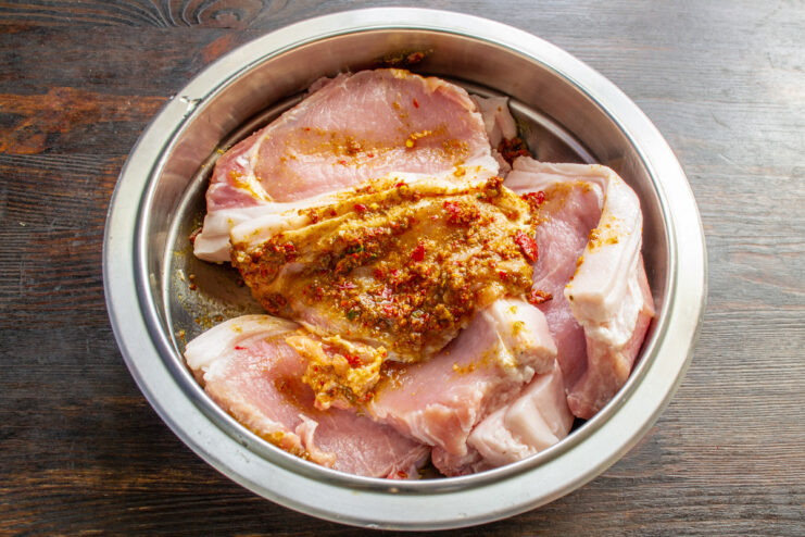Step 3: Marinating the Pork Loin Chops Sliced pork loin chops in a bowl being coated with a red spice marinade.