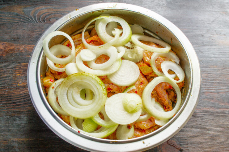 Step 4: Adding Sliced Onions to the Marinating Pork Sliced onions being added to the bowl with marinated pork loin.