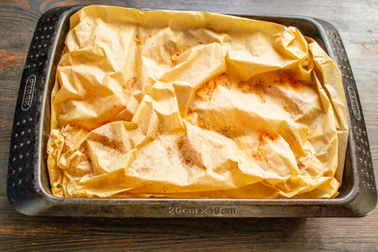 Step 9: Covering the Dish with Parchment Paper The baking dish with pork, vegetables, and cheese being covered with another sheet of parchment paper.