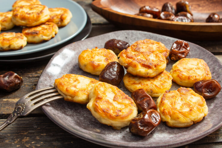 A plate of golden-brown ricotta syrniki with dates, garnished with fresh mint.