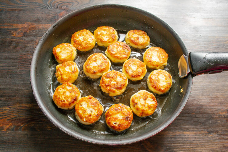 Flipping Syrniki to Achieve a Golden-Brown Crust Ricotta syrniki being fried to a perfect golden-brown color in a pan.