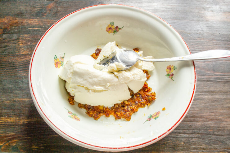 Combining Ricotta and Dates for Syrniki Batter A white bowl containing chopped dates with a spoonful of ricotta cheese being added.