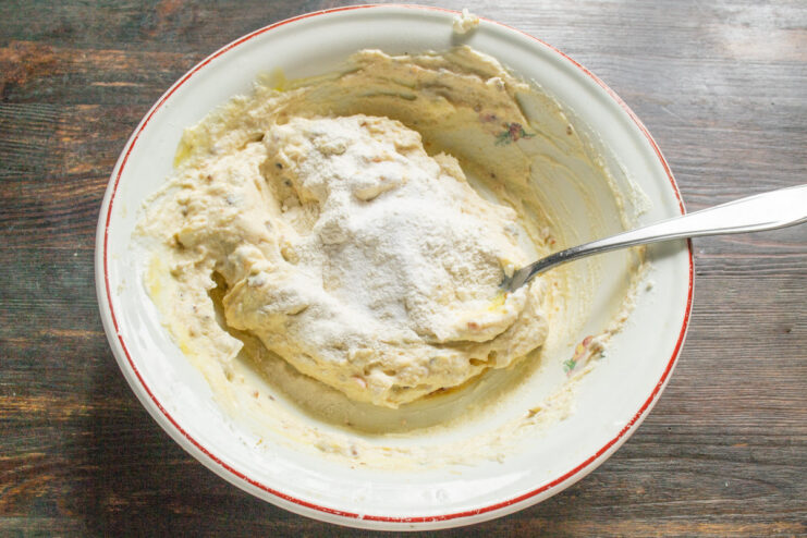 Adding Flour to the Ricotta and Date Mixture Adding a spoonful of wheat flour to the bowl with the syrniki batter.