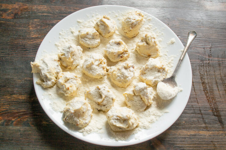 Coating Syrniki in Flour Before Shaping Small portions of syrniki dough being generously coated with flour on a plate.
