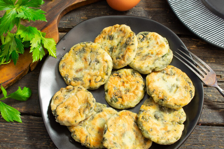 A plate of golden-brown syrniki with cottage cheese and spinach, served with a white sauce and fresh herbs.
