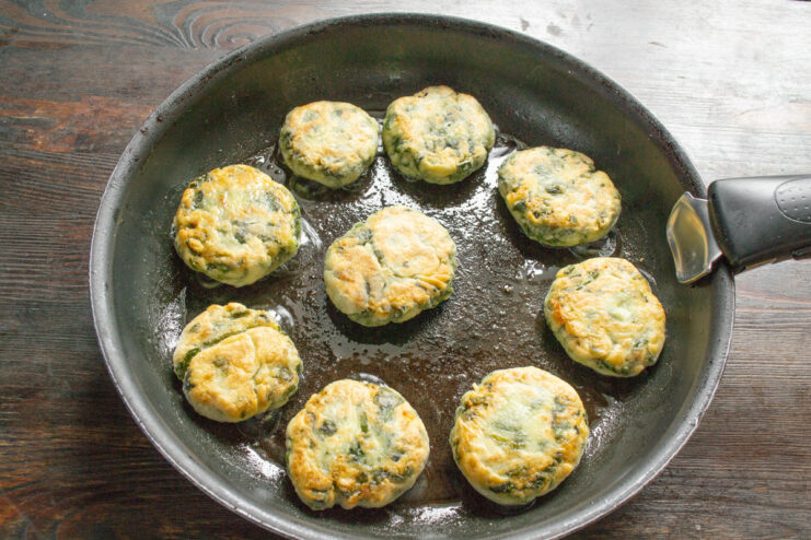 Cooking the other side of the syrniki until golden. A spatula flipping golden-brown syrniki in a frying pan.