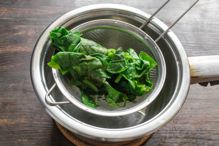 Make sure to remove all excess water from the spinach. A hand squeezing excess water from a ball of cooked spinach over a sink.