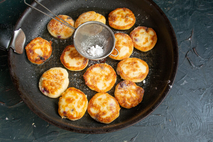 A finishing touch: dusting Syrniki with powdered sugar Dusting the freshly fried syrniki with powdered sugar while they are still in the pan.
