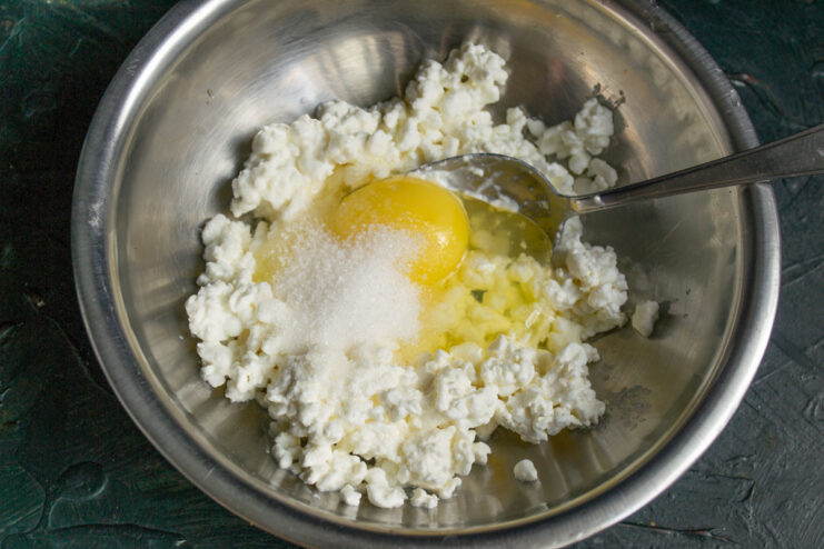 Seasoning the Syrniki batter with sugar, vanilla, and salt Adding sugar, vanilla sugar, and salt to the tvorog and egg mixture in a bowl.