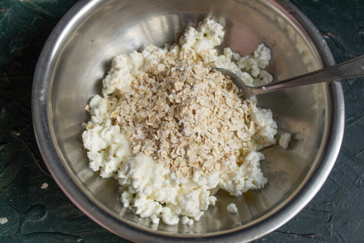 Mixing in quick-cooking rolled oats for texture Adding quick-cooking rolled oats to the syrniki batter in a bowl.