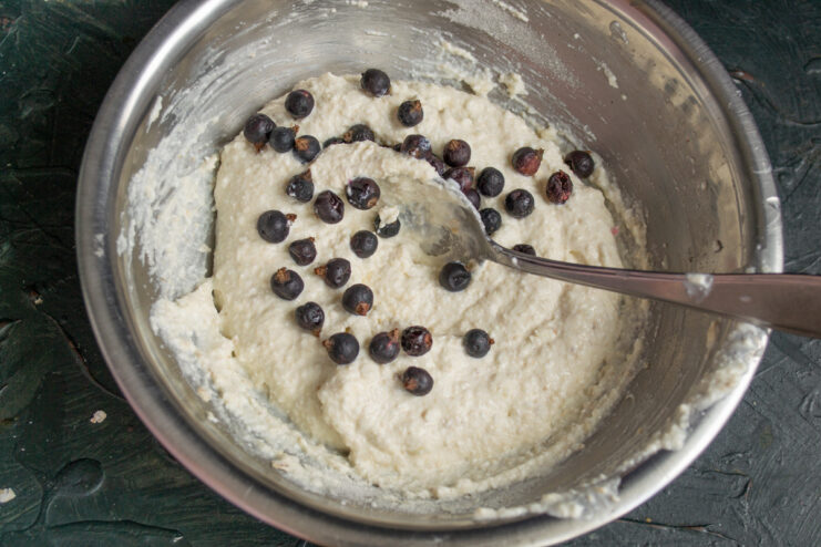 Folding black currants into the Syrniki batter A handful of black currants being added to the smooth syrniki batter.