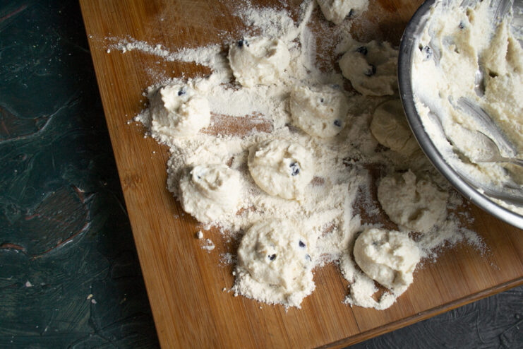 Forming the Syrniki patties in flour Using a teaspoon to portion the syrniki batter onto a floured surface.