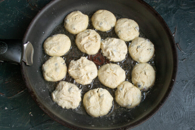 Frying Syrniki until golden brown on one side Syrniki patties frying in a hot skillet on one side.