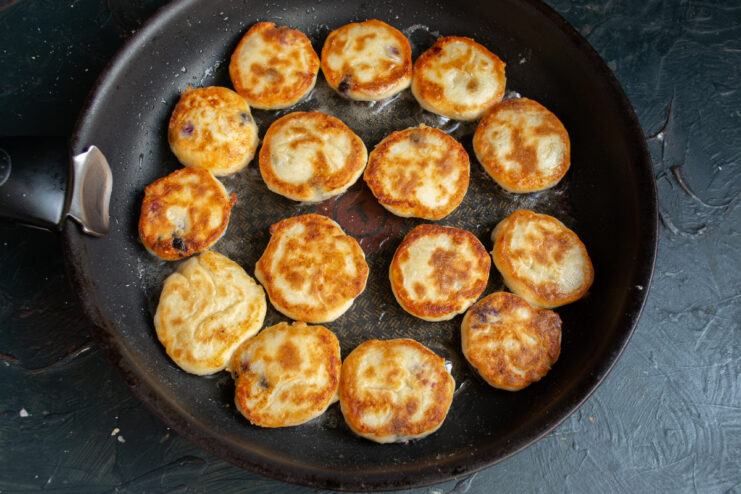 Flipping the Syrniki to cook the other side Flipping the syrniki in the skillet to cook them until golden brown on both sides.