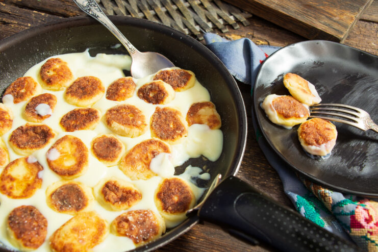 A plate of golden-brown syrniki (farmer's cheese pancakes) served in a pool of yellow custard.
