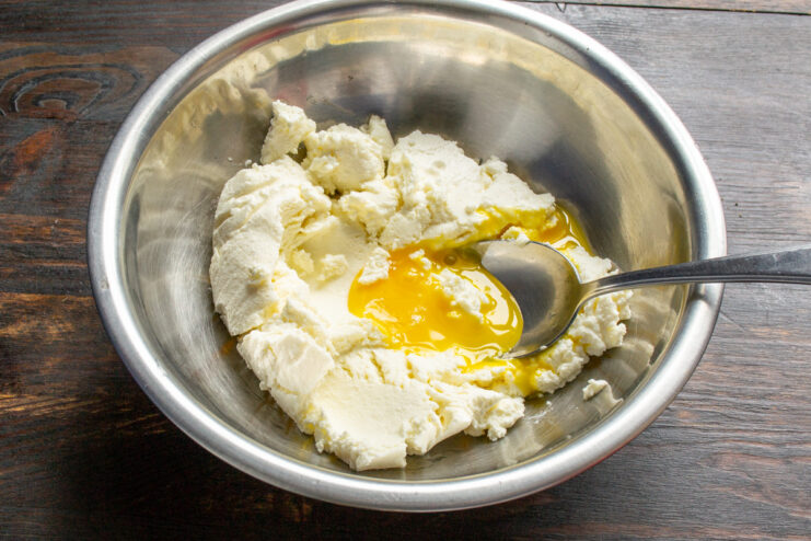 Step 1: Combining the main ingredients for the syrniki dough A white bowl containing farmer's cheese, an egg, salt, and sugar, ready to be mixed for syrniki.