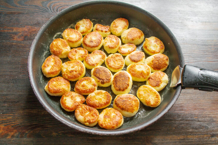 Flipping the syrniki to cook the other side until golden Flipping golden-brown syrniki in a skillet with a spatula.