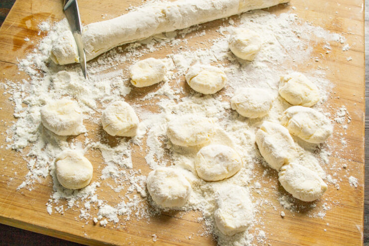 Cutting the syrniki dough into individual portions Cutting a log of syrniki dough into small, thick rounds on a floured surface.