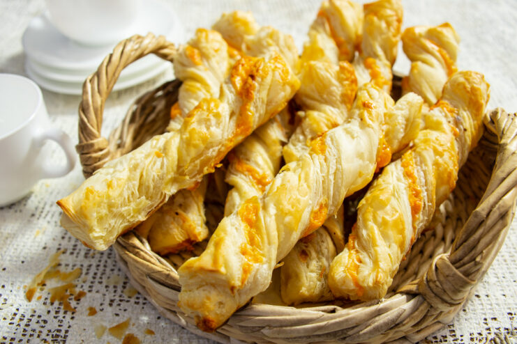A plate of golden-brown, twisted puff pastry cheese sticks ready to be served.